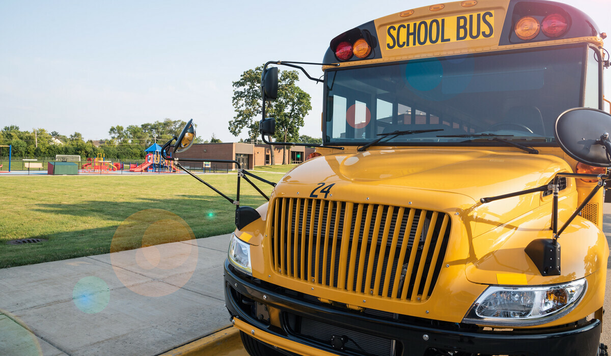 A close up of the front of a school bus that is parked in front of a school on a sunny morning.